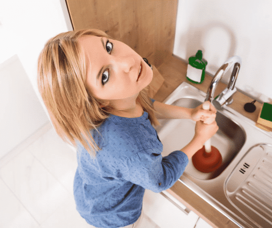 woman using a plunger to unclog a kitchen sink