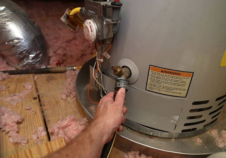 Hand attaches hose to a home water heater to perform maintenance