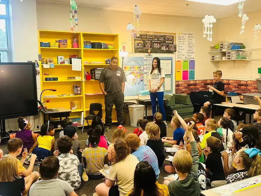 The Mink Plumbing team presenting to a group of children sitting on the floor in a school library at Whitehouse ISD Career Day.