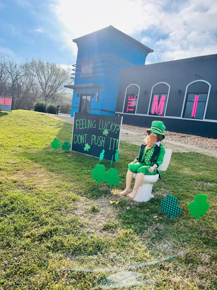 Leprachaun sitting on toilet outside of The Mink Plumbing.