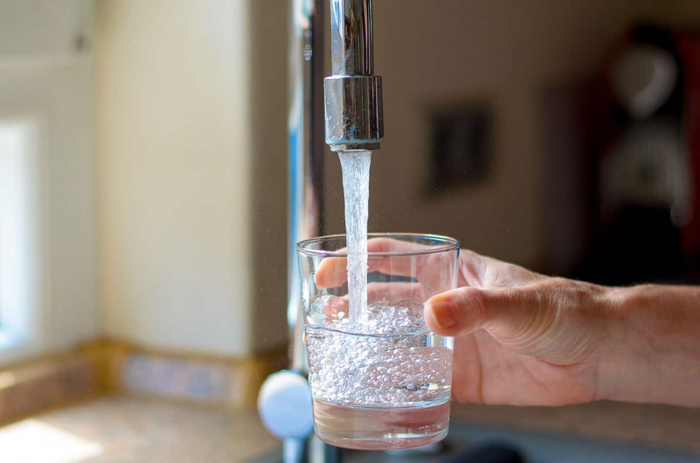 person filling up glass of water at kitchen sink